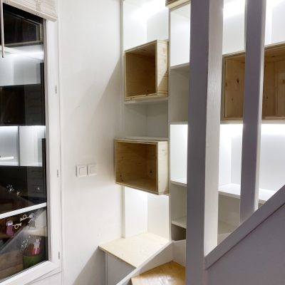 Bibliothèque derrière escalier existant. Mélaminé blanc et épicéa. Bandeaux Led dans les niches.